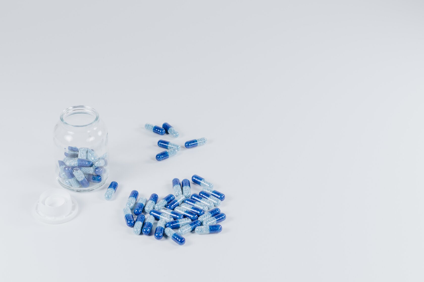 Blue and white capsules beside a glass bottle