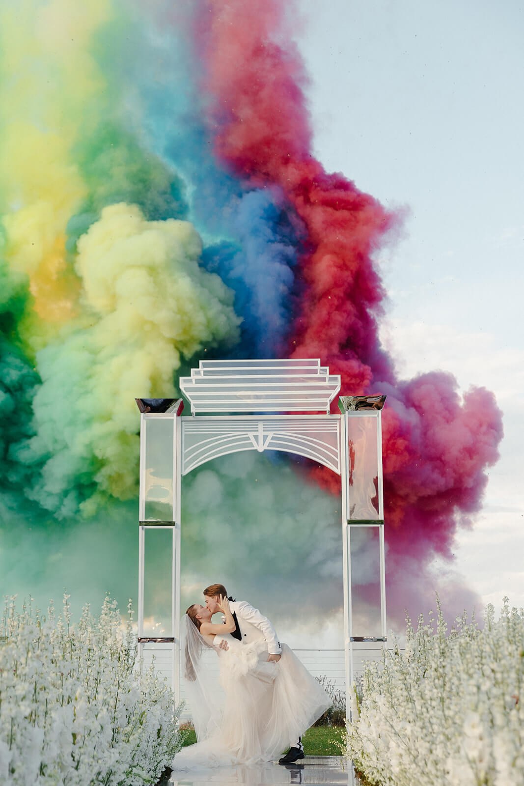 Wedding couple beneath a white arch against coloured smoke Wedding couple beneath a white arch against coloured smoke